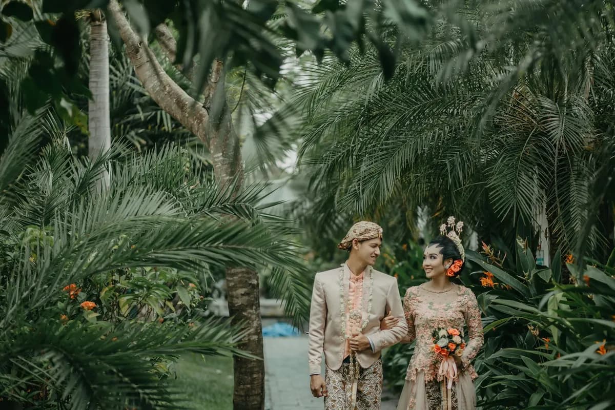 Pasangan berbusana pengantin Jawa berjalan di taman